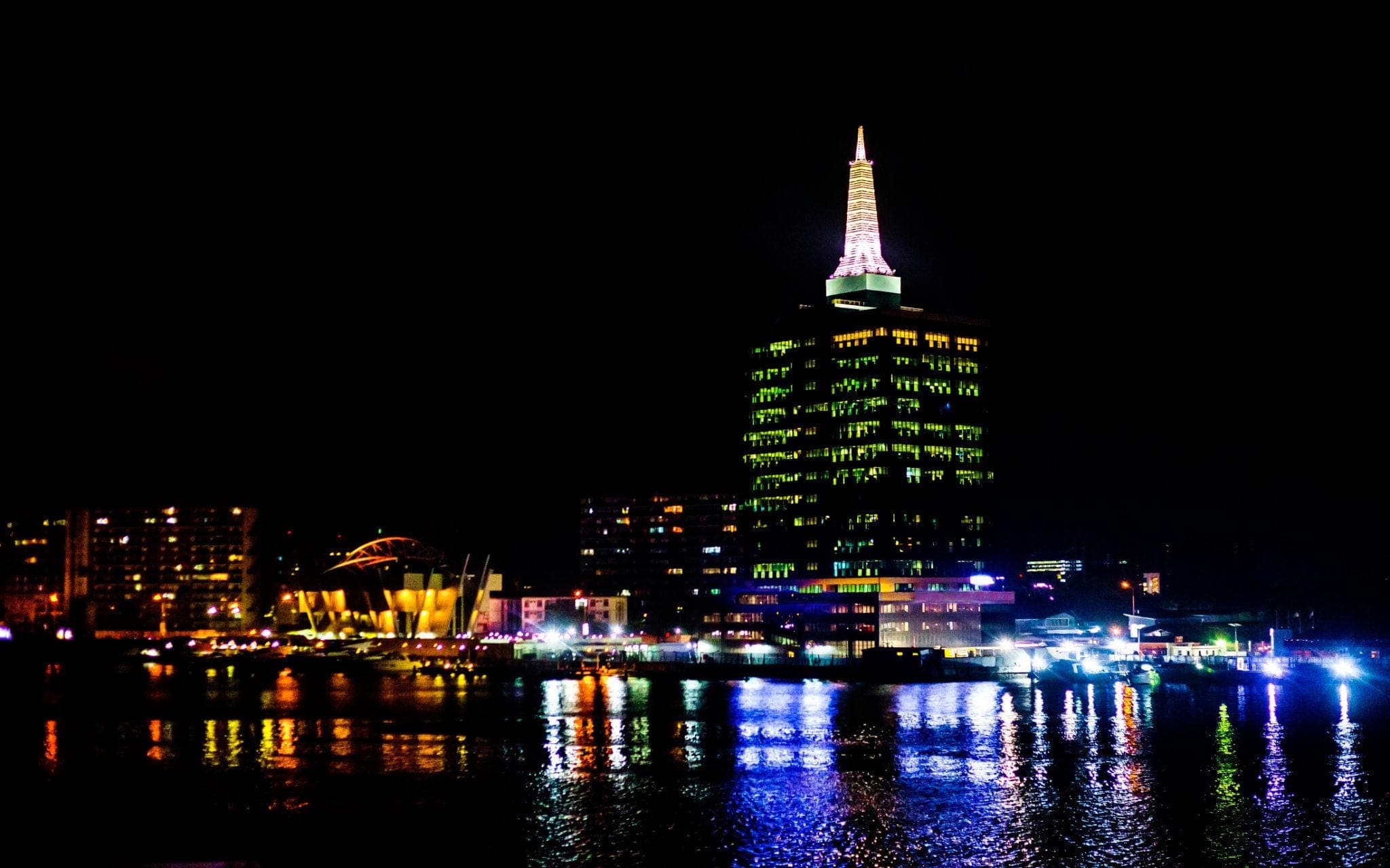 Nighttime city skyline with reflections on water.